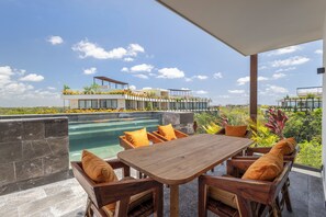 A modern outdoor dining area with a pool, wooden furniture, and a view of a residential complex. - Luxury Jungle Penthouse. Private Rooftop, Pool & High-Speed WiFi (Tulum)