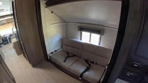 A compact RV interior with a sofa bed, a small window, and a kitchenette area. - Kenai Riverfront RV Camping & World Class Fishing. (Soldotna)