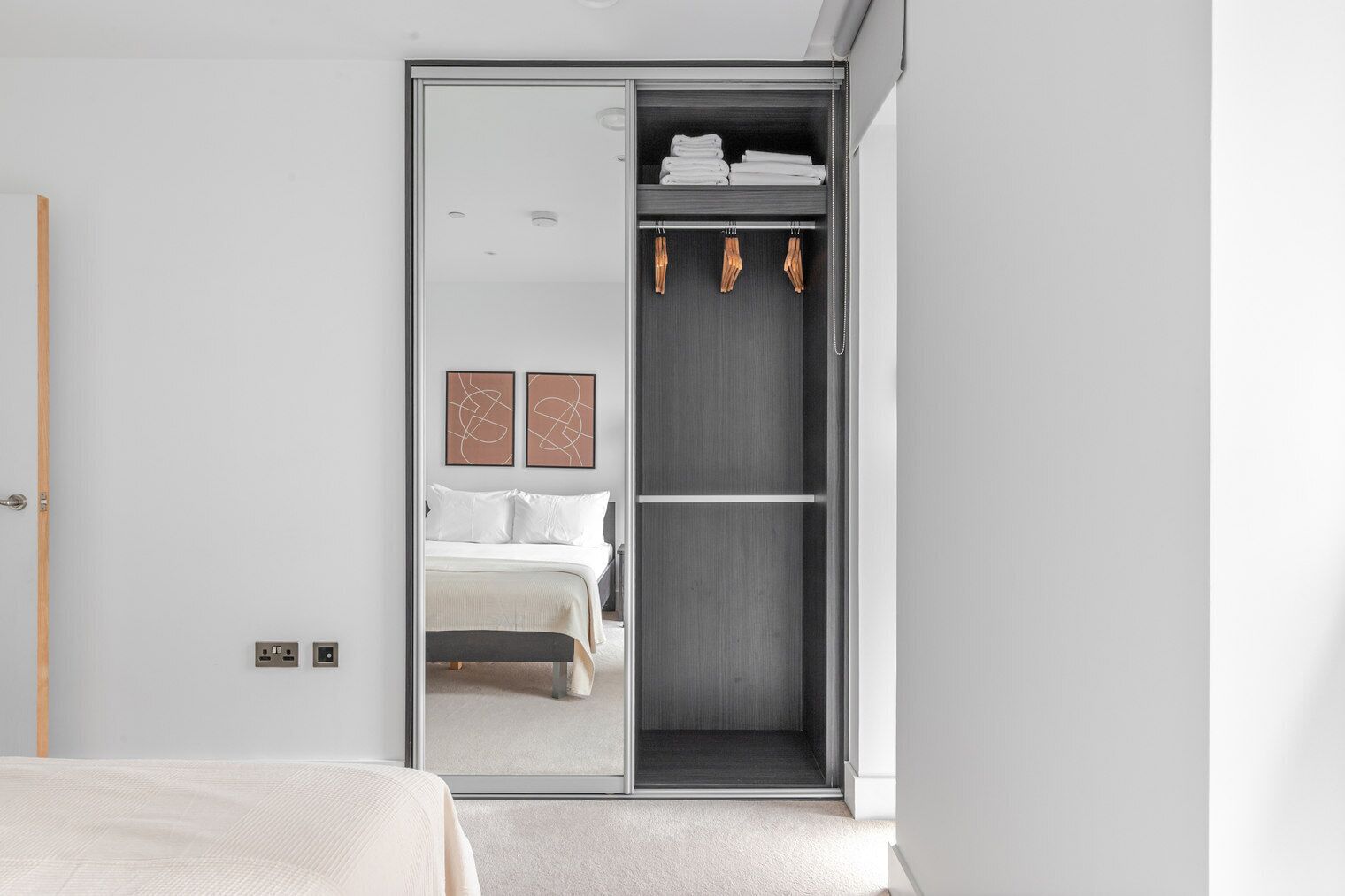 Een moderne slaapkamer met een grote schuifdeurkast, een bed met witte lakens en twee abstracte kunstwerken aan de muur.