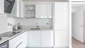 A modern kitchen with white cabinetry, a stainless steel sink, and a built-in oven. - Blueground | Whitechapel, fitness center, nr Tower of London (London)