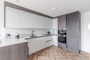 A modern kitchen with white cabinets, a marble countertop, a coffee machine, and a built-in oven. - Blueground | Southwark, rooftop, nr Tower Bridge (London)