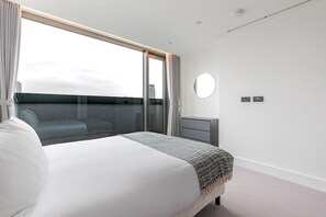 A modern hotel room with a large bed, a small bedside table, a round mirror, and a view of the city through a large window. - Blueground | Southwark, rooftop, nr Tower Bridge (London)