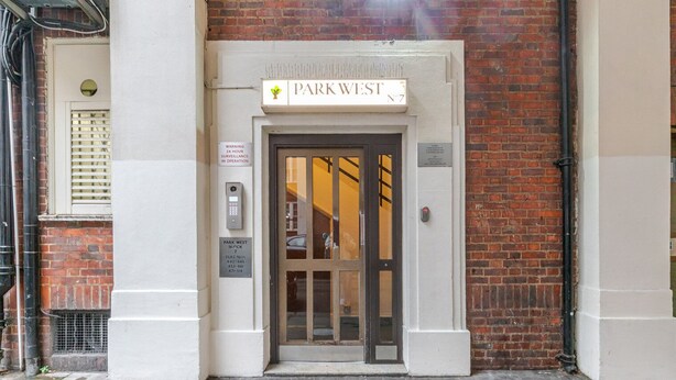 Ein Gebäudeeingang mit einem Schild, auf dem "Park West" steht, und einem Hinweis auf Videoüberwachung rund um die Uhr.