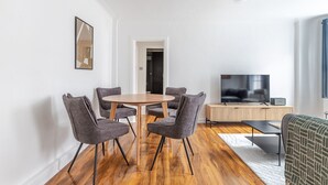Ein modernes Wohnzimmer mit einem runden Holztisch und vier grauen Stühlen, einem Flachbildfernseher und einem Holzschrank.