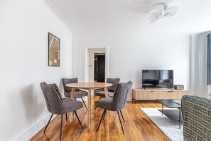 A modern living room with a round wooden table and four grey chairs, a flat-screen TV, and a wooden cabinet. - Blueground | St George's Fields, view, nr Hyde Park (London)