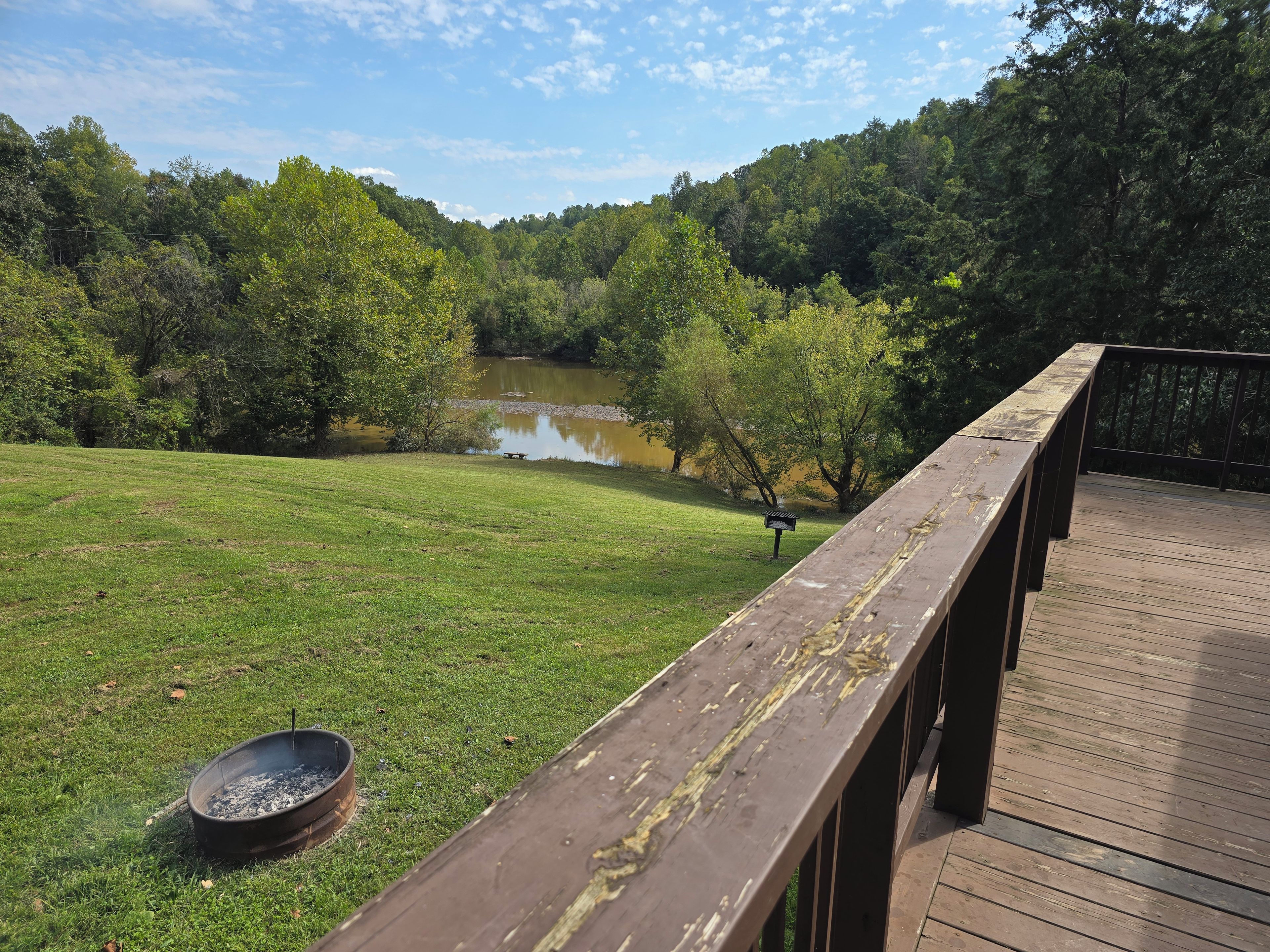 A wooden deck overlooking a grassy area with a pond and dense trees in the background.
