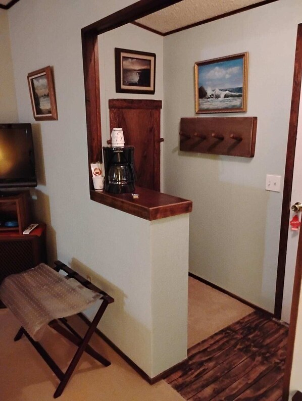 Una kitchenette pequeña con cafetera, televisor y un banco.