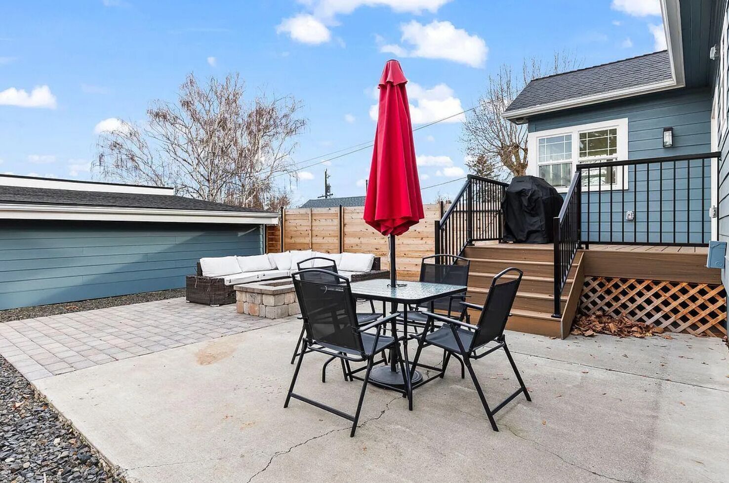 A patio with a table and chairs, a red umbrella, and a covered barbecue area.