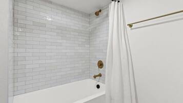 Ein Badezimmer mit weißen Fliesenwänden, einer weißen Badewanne und einer Duschvorhang.
