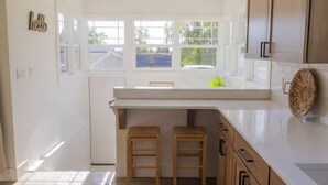 Une cuisine moderne avec une grande fenêtre, des tabourets en bois et un panier tressé posé sur le plan de travail.