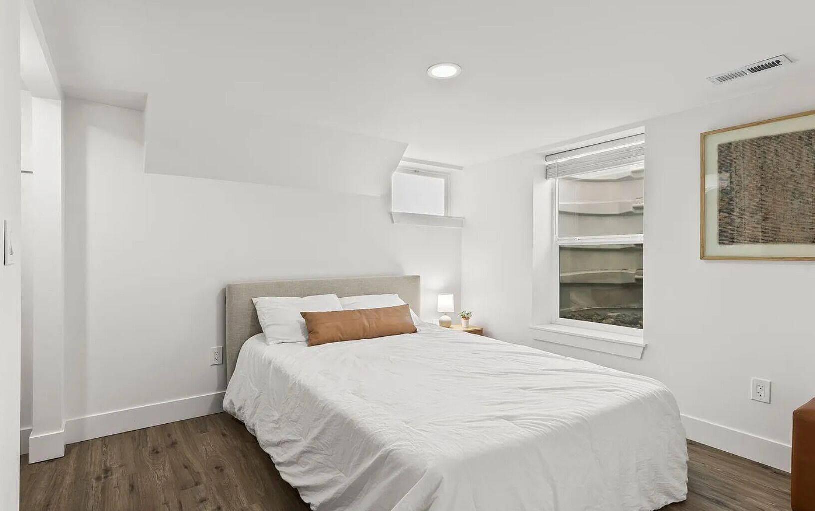 A bedroom with a bed, a nightstand, a window with blinds, and a framed picture on the wall.