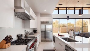 A modern kitchen with a stainless steel refrigerator, a gas stove, and a large island with a sink. - Nyx - Near Troon North Golf & Scottsdale Quarter (Scottsdale)