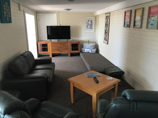 A living room with a TV on a wooden cabinet, a sofa, a coffee table, and a carpeted floor. - Blackwood Hideaway (Augusta)