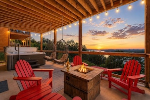 Une terrasse extérieure couverte avec un foyer, des fauteuils Adirondack rouges, une table en bois et un jacuzzi.
