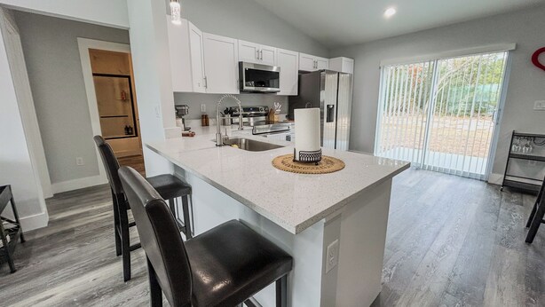 A modern kitchen with white cabinetry, stainless steel appliances, and a central island with bar stools. - 5.0 Rated 3BR Retreat • Gated Patio • Near WEC (OCALA)