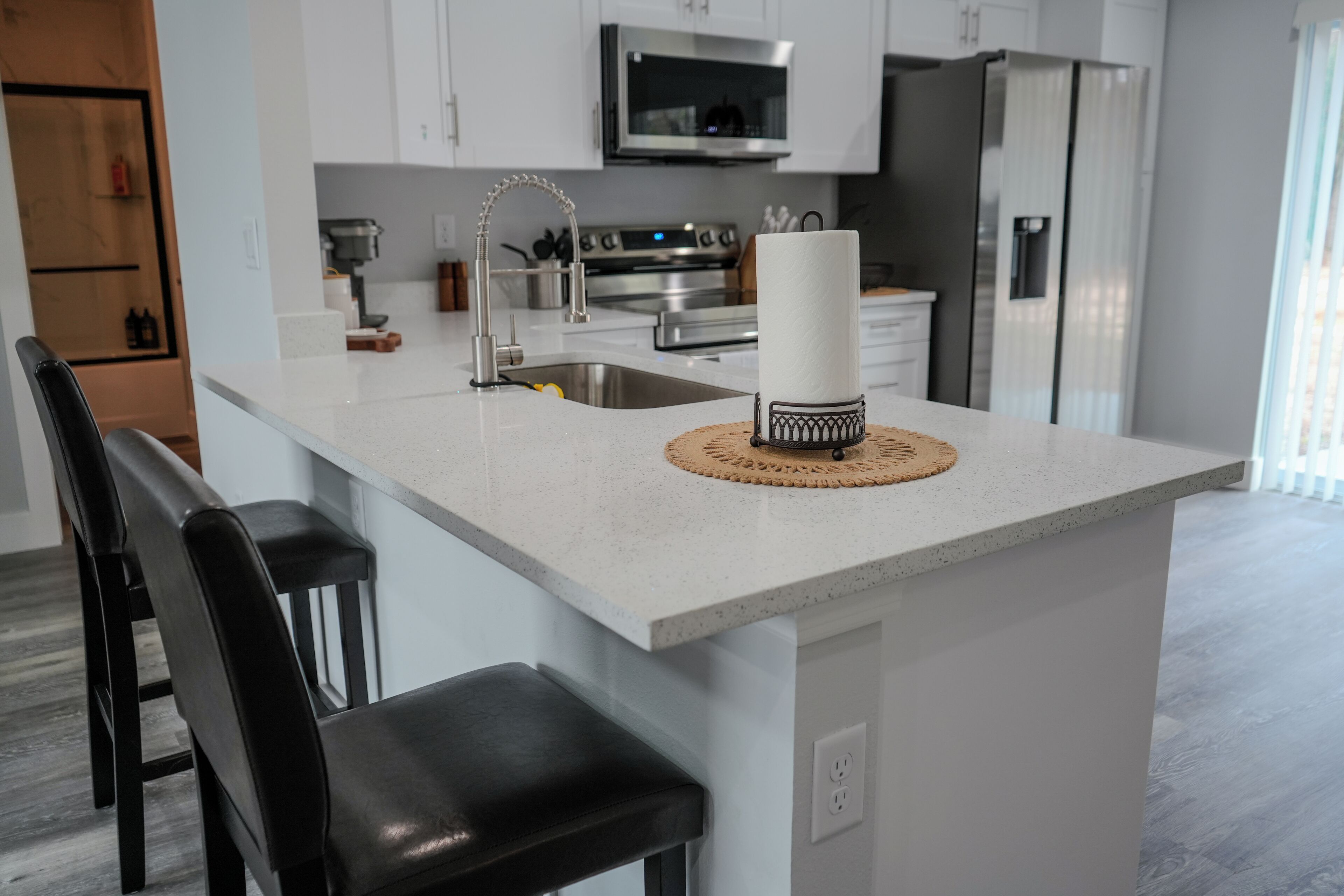 Een moderne keuken met witte kasten, roestvrijstalen apparatuur en een centraal eiland met barkrukken.