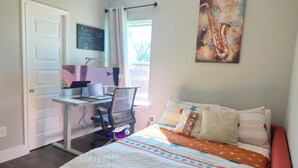 A bedroom with a bed, a desk with a computer, a chair, a window with curtains, and a painting on the wall. - Private Pool at Pershing Flat. 3BR Sleeps 9. 10 mins from NRG . Huge backyard (Houston)
