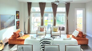 A living room with a white sofa, two armchairs, a ceiling fan, and large windows with curtains. - Private Pool at Pershing Flat. 3BR Sleeps 9. 10 mins from NRG . Huge backyard (Houston)