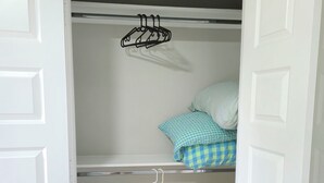 A walk-in closet with a hanging rod and a shelf, a bed with a checkered blanket, and a wooden floor. - Private Pool at Pershing Flat. 3BR Sleeps 9. 10 mins from NRG . Huge backyard (Houston)
