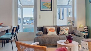 Un salon comprenant un canapé, des fauteuils, une table à manger et offrant une vue dégagée grâce à de grandes fenêtres.