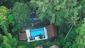 Luftaufnahme eines Resorts mit einem zentralen Schwimmbecken, umgeben von sechs rechteckigen Gebäuden, vermutlich Gästezimmern, und einem Weg, der zu einem kleinen Steg führt.