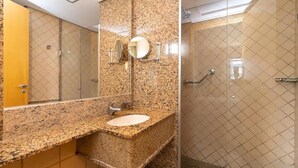 A bathroom with a granite countertop sink, a mirror, and a shower with a glass door. - Flat Let's Idea - Centro de Brasília (Brasília)