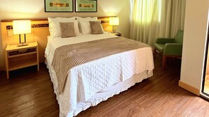 A hotel room with a large bed, two bedside tables with lamps, a green chair, and a window with curtains. - Flat Let's Idea - Centro de Brasília (Brasília)