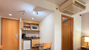 A compact hotel room with a kitchenette, a dining area with a table and chair, a bed, and a ceiling-mounted air conditioner. - Flat Let's Idea - Centro de Brasília (Brasília)