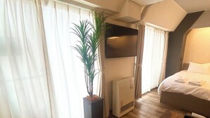 A hotel room with a bed, a bedside table, a potted plant, a heater, and a large window with curtains. - TOWN ROYAL 701 (Sapporo)