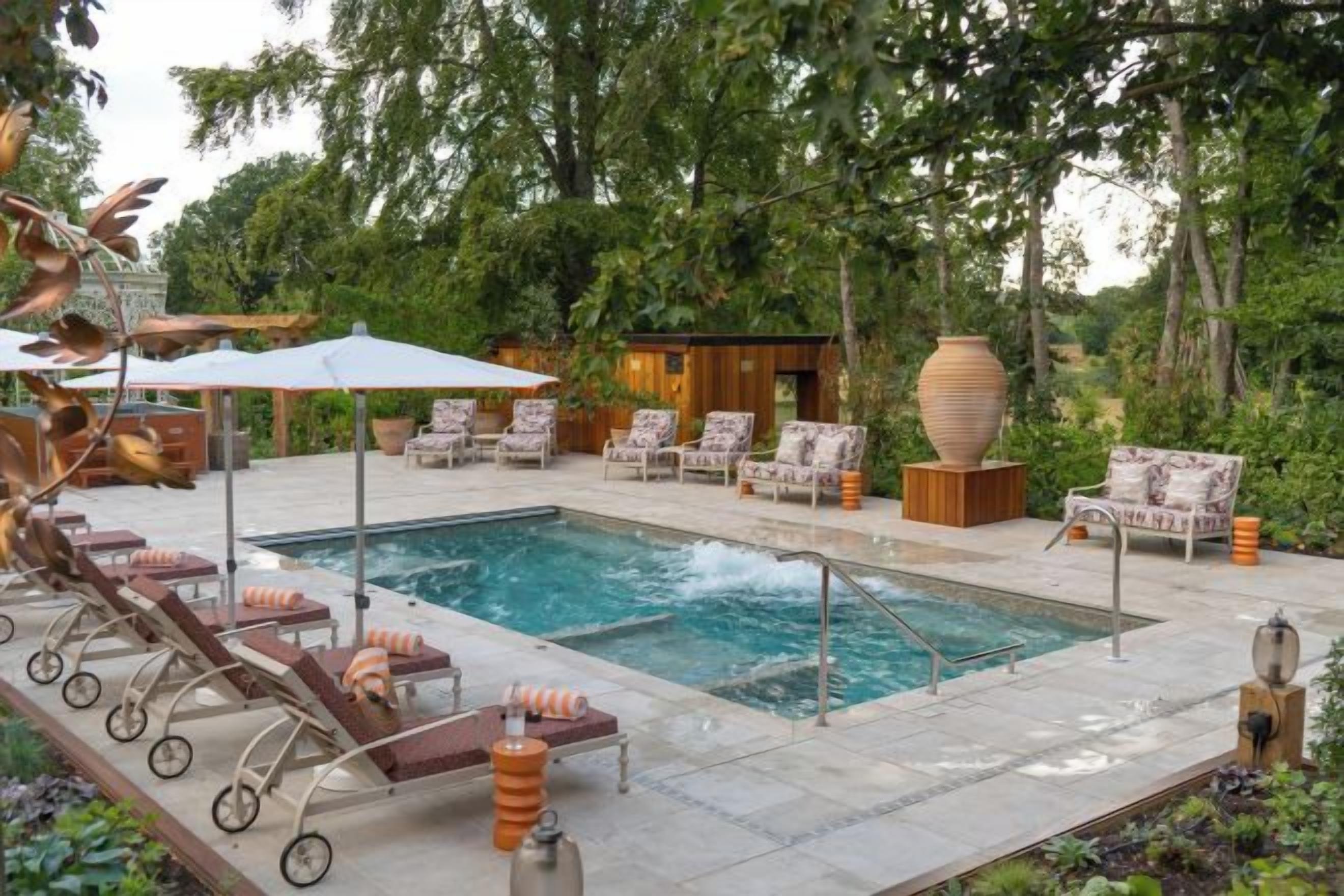 A pool area with lounge chairs and umbrellas, surrounded by greenery.