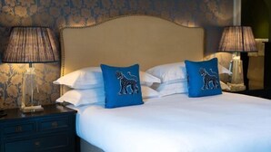 Un lit bien fait, orné de deux coussins bleus, une table de chevet en bois avec une lampe, et un papier peint à motifs.