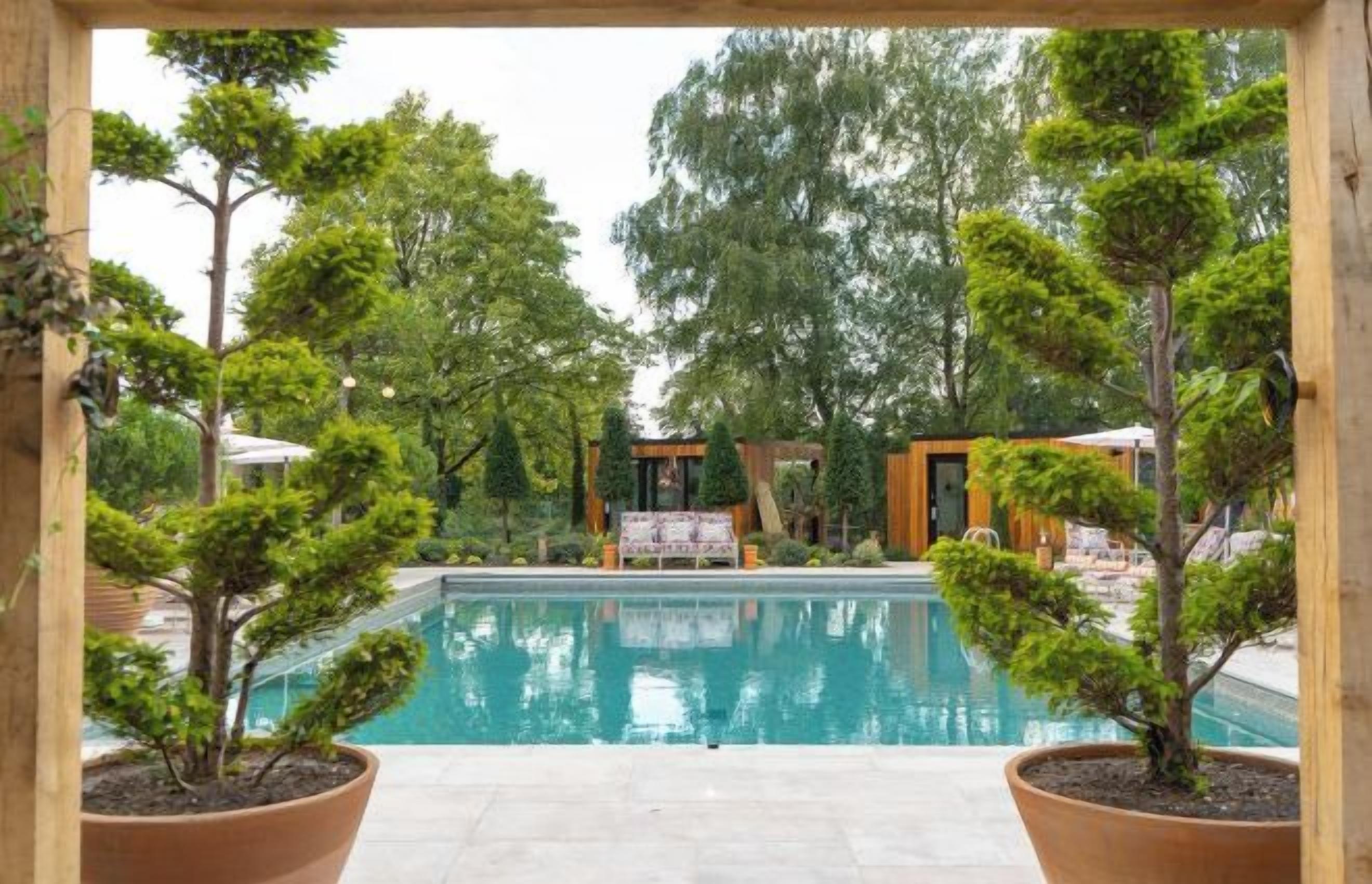 A pool area with potted trees, a wooden pergola, and a lounge chair.