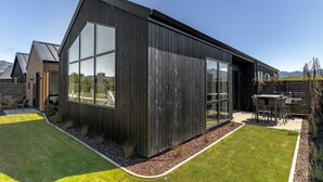 A modern building with large windows, a patio area with outdoor furniture, and a view of the surrounding landscape. - Jacks Point Ultimate Family Escape With Remarkable Views (Queenstown)