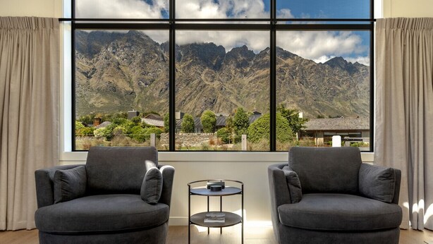 A room with two grey armchairs facing a large window overlooking a mountainous landscape. - Jacks Point Ultimate Family Escape With Remarkable Views (Queenstown)