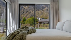 A bedroom with a large bed, a view of mountains, and a window with curtains. - Jacks Point Ultimate Family Escape With Remarkable Views (Queenstown)