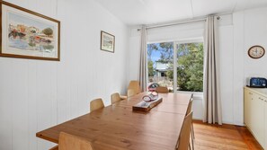 Un coin repas avec une table en bois, des chaises, une horloge et une vue sur l’extérieur grâce à une grande fenêtre.