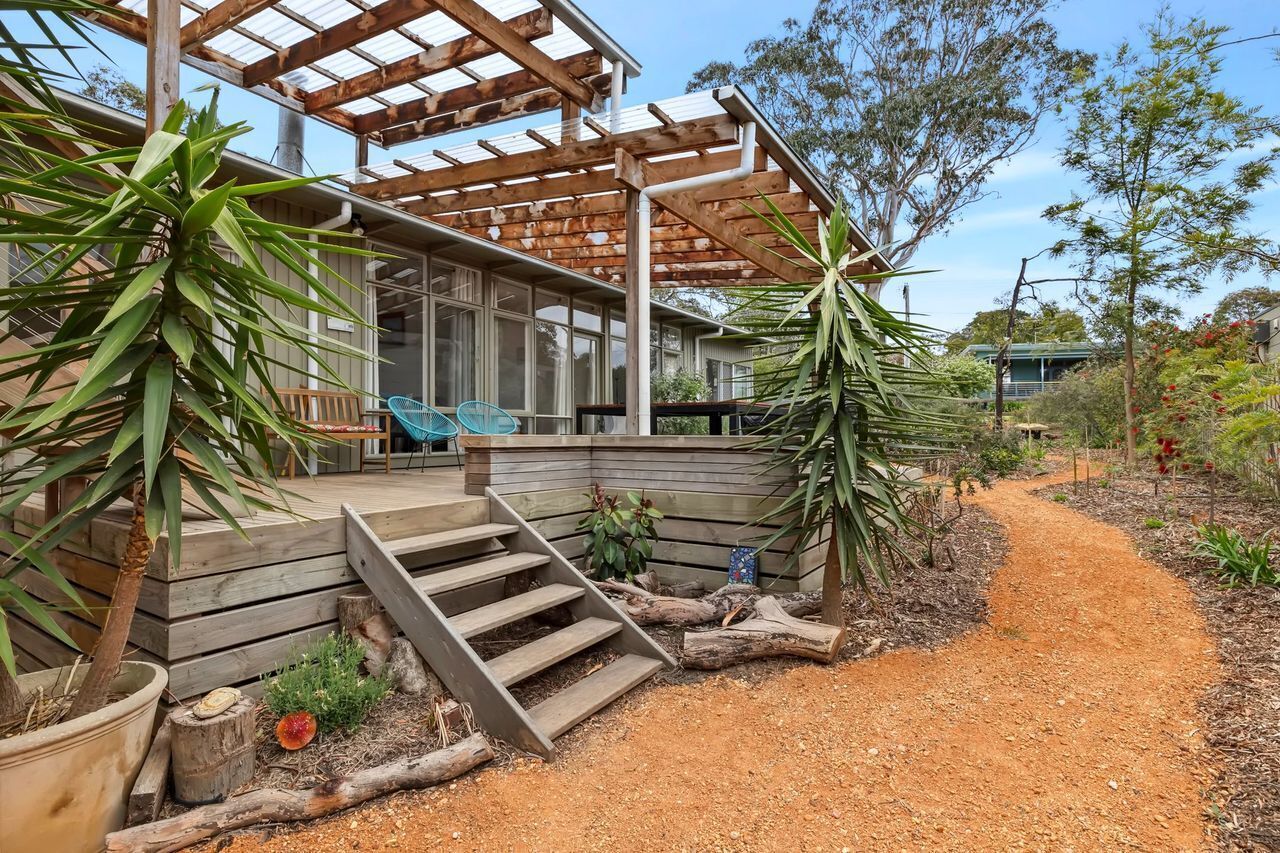 A modern house with a wooden deck, a staircase leading to the entrance, and a garden with various plants.