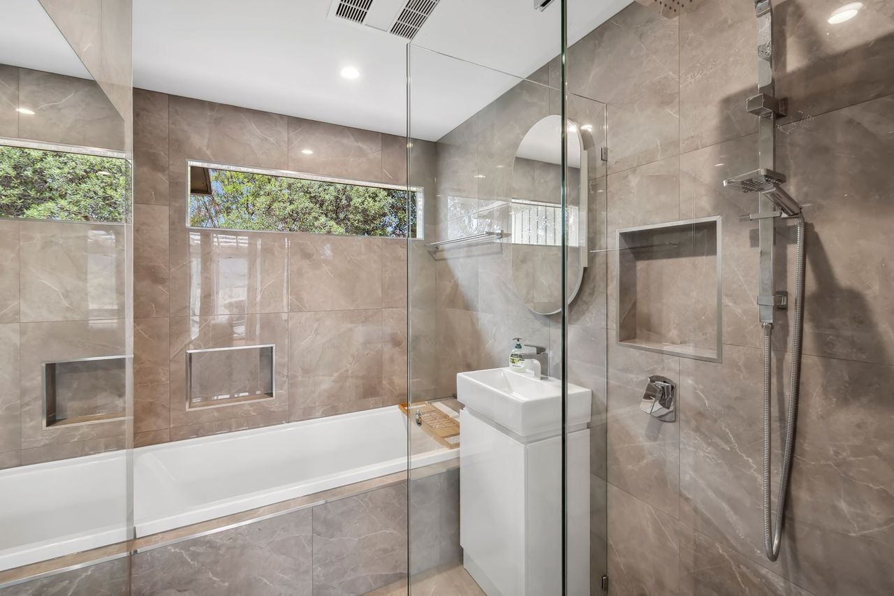 A modern bathroom with a glass-enclosed shower, a white bathtub, and a sink.
