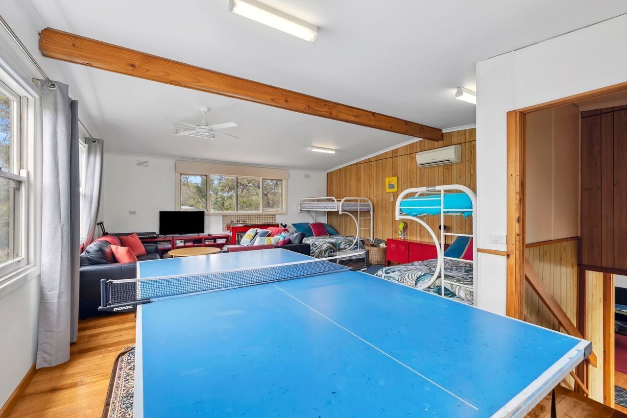 Ein Zimmer mit Tischtennisplatte, einer Couch mit Kissen, einem Fernseher und einer Holzbalkendecke.