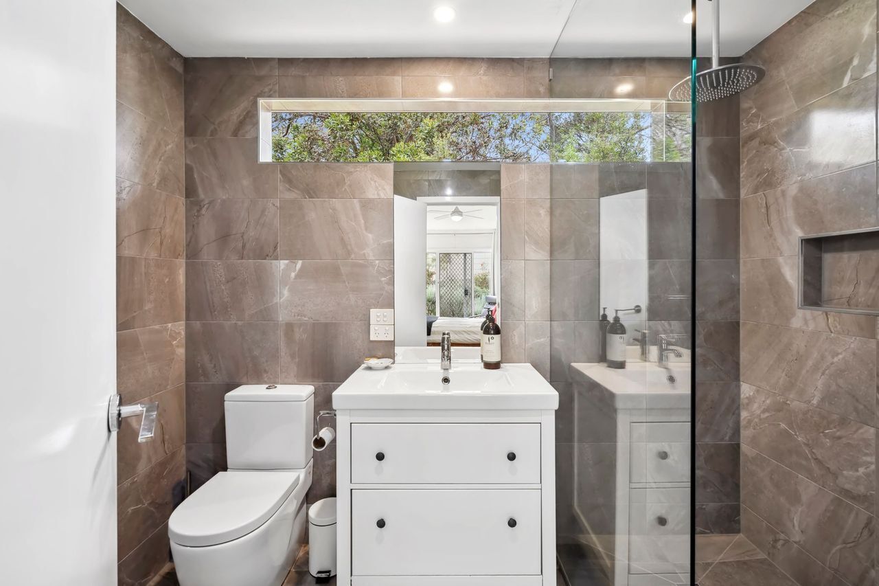 Ein modernes Badezimmer mit Toilette, Waschbecken und Duschbereich, ausgestattet mit Marmorfliesen und einer Glasdusche.