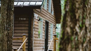Eine Holzhütte mit der Nummer 7908 an der Tür, einer Veranda mit Holzbalkonen und einem kleinen Fenster mit Vorhang.