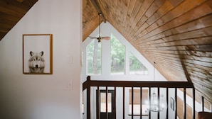 Ein Zimmer mit schräg verlegtem Holzboden, einem gerahmten Bild an der Wand und Blick ins Freie durch große Fenster.