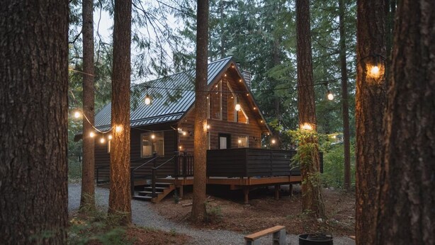 Eine rustikale Holzhütte mit einer Holzterrasse, umgeben von hohen Bäumen und Lichterketten.