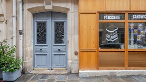 Fachada de edificio con una pastelería llamada "Pâtisserie le petit COLORVA", que presenta una puerta azul con diseños intrincados y una entrada con contraventanas de madera.