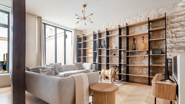 Un salón moderno con sofá, mesa de centro y pared de piedra con estantes empotrados.