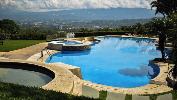 Una piscina gran i corbada amb una font, envoltada de paisatges ben cuidats i palmeres.
