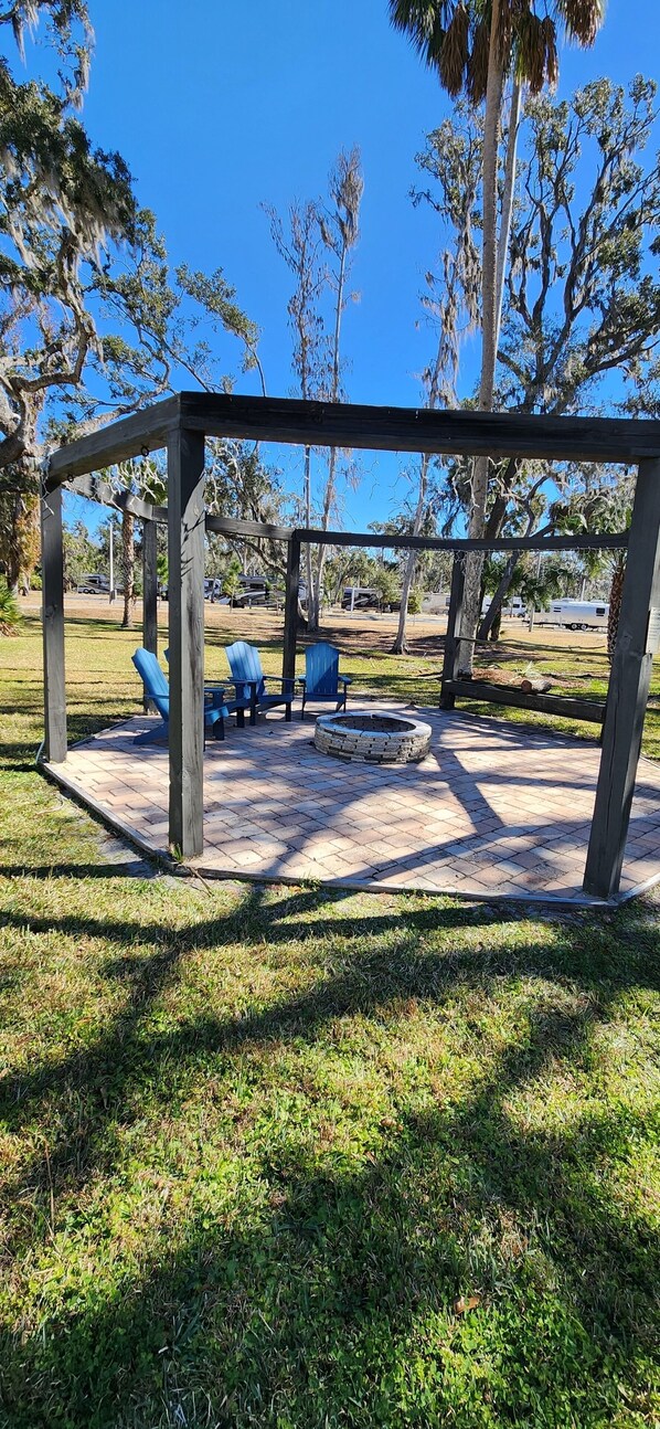 A gazebo with blue chairs and a fire pit in a park.