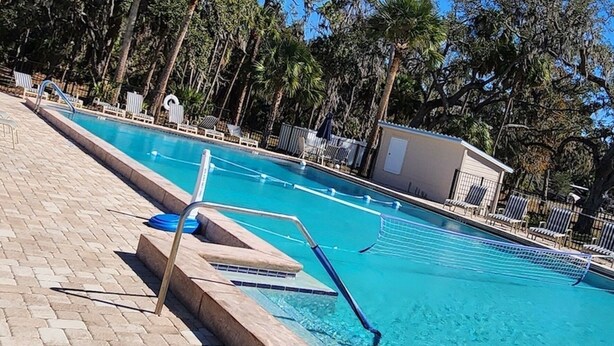 En swimmingpool med ett kaklat poolområde, omgiven av palmer och en klarblå himmel.