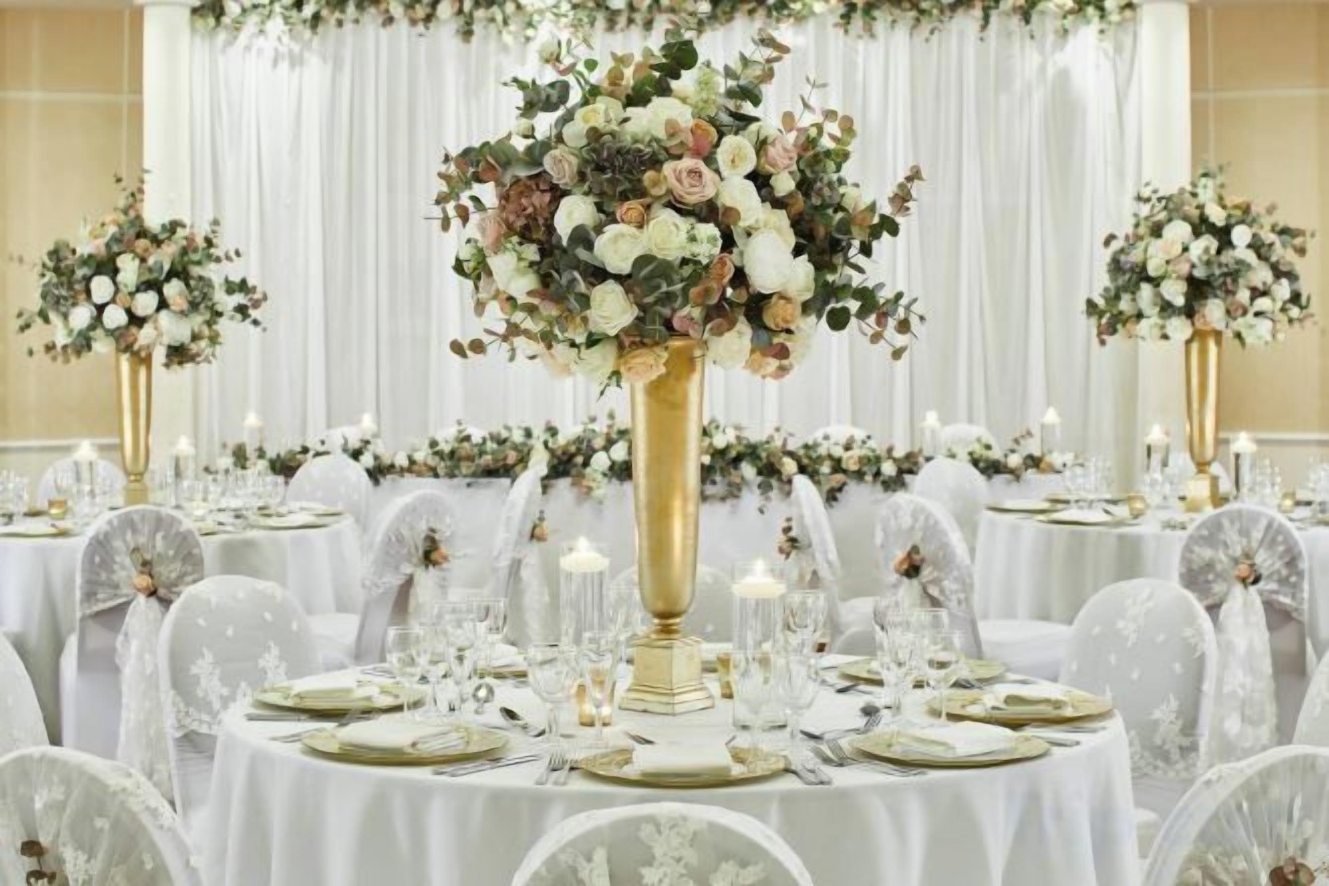 A banquet hall with round tables set for a formal event, each with a centerpiece and candle.