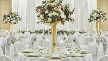 A banquet hall with round tables set for a formal event, each with a centerpiece and candle.